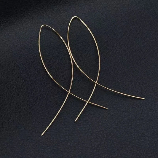 Aramat Jewels goudkleurige doortrek oorbellen in een minimalistische geometrische visvorm op een zwarte achtergrond.