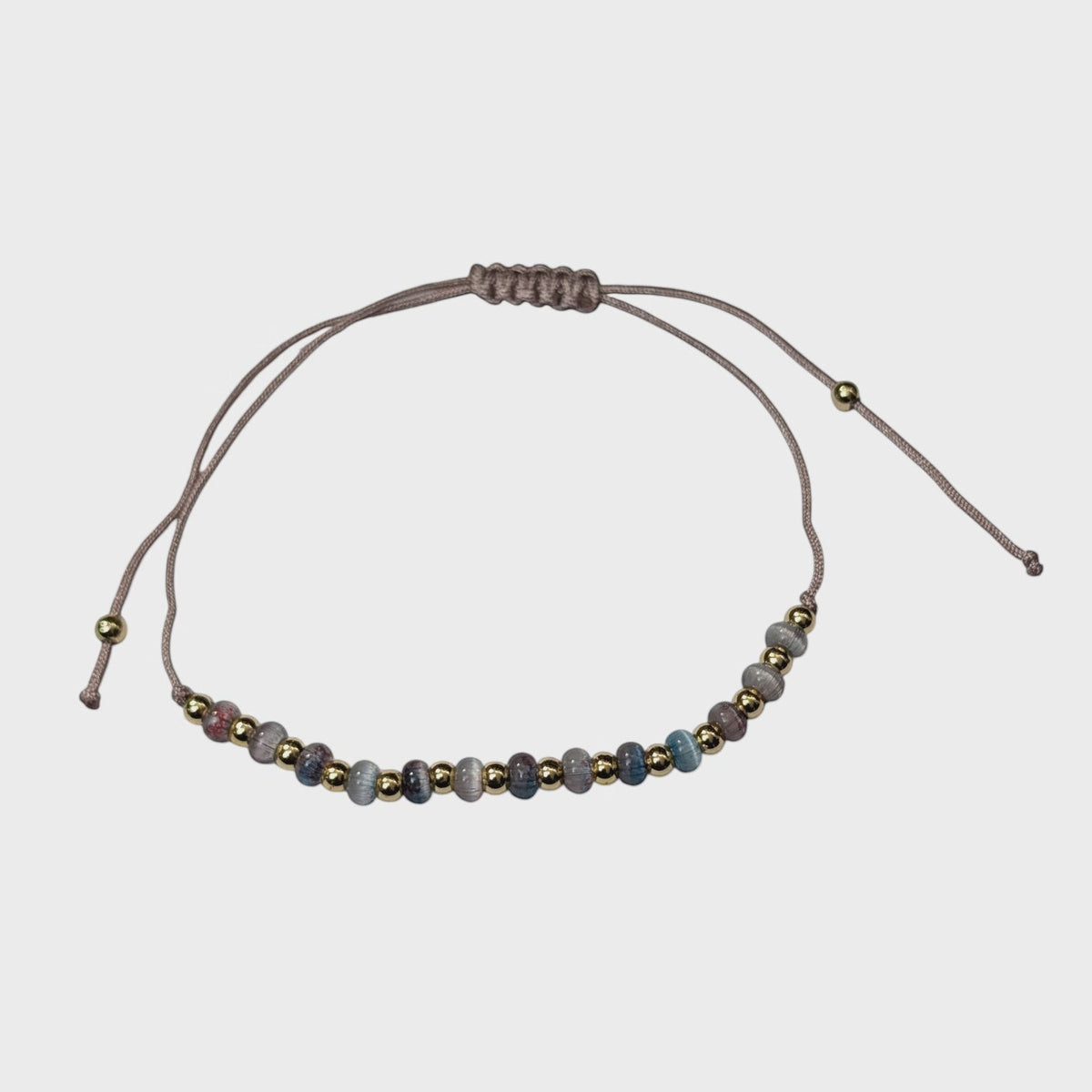 Aramat Jewels verstelbaar enkelbandje met grijze cats eye kralen en goudkleurige accenten op een taupe touwtje.