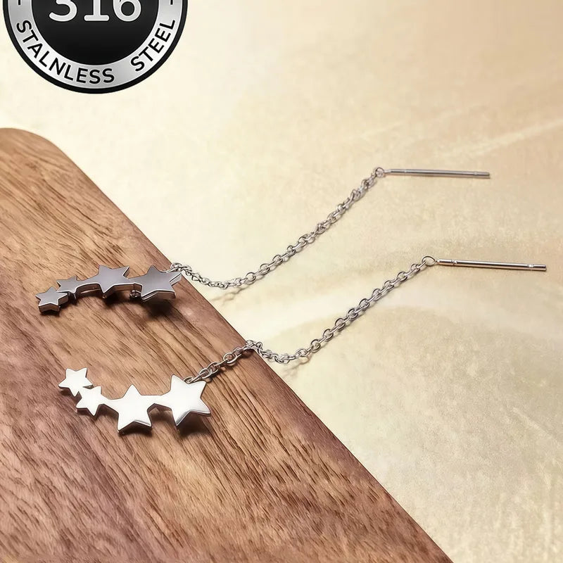 Aramat Jewels zilverkleurige doortrek oorbellen van RVS met sterretjes motief op een houten ondergrond