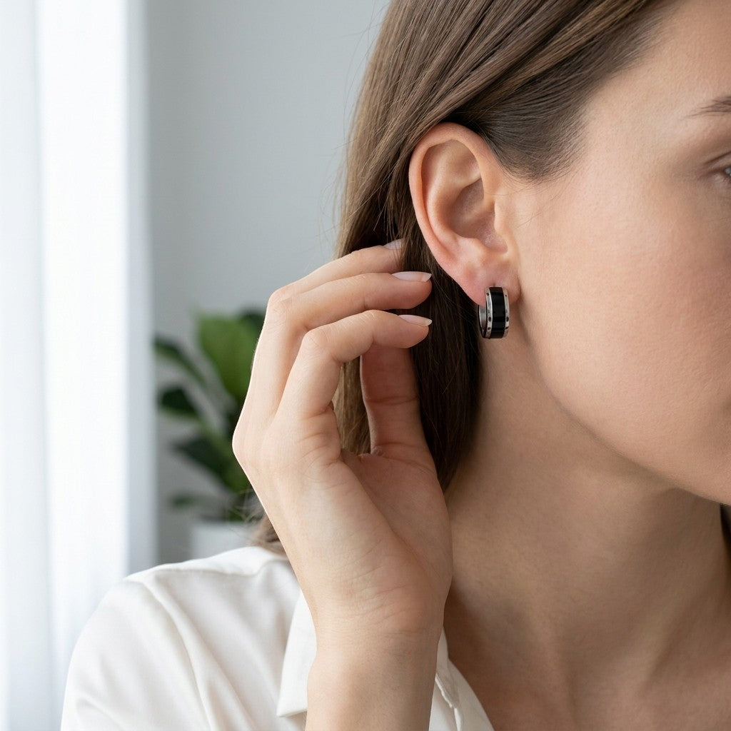 Aramat Jewels bicolor stainless steel hoop earrings, 13x7mm, with a glossy black and silver finish. A woman's ear is shown with the earring.