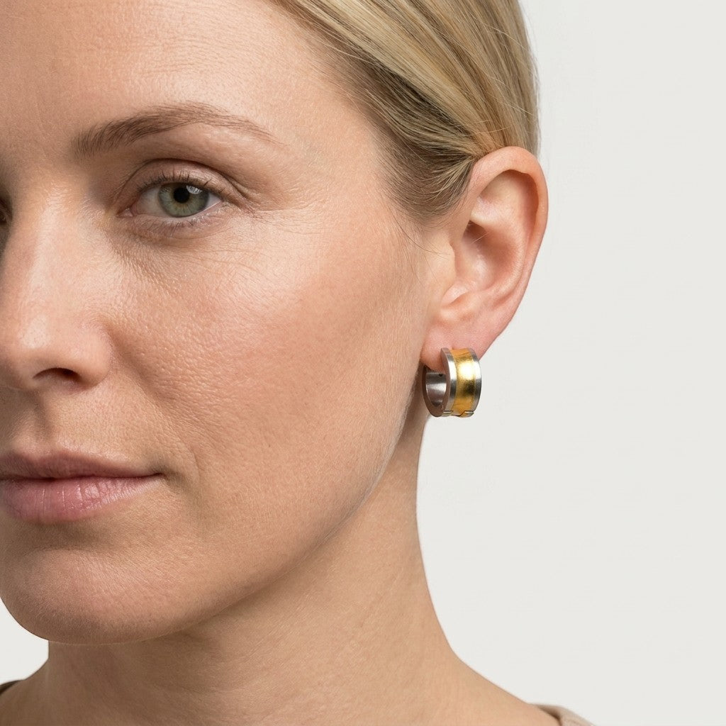 Aramat Jewels bicolor stainless steel hoop earrings with a wide gold stripe, 13mm diameter, worn by a model.