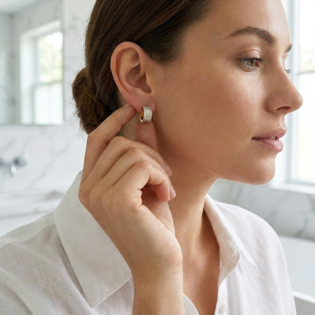 Aramat Jewels matte bicolor stainless steel hoop earrings, 13x7mm, in silver and gold tones, worn by a woman.