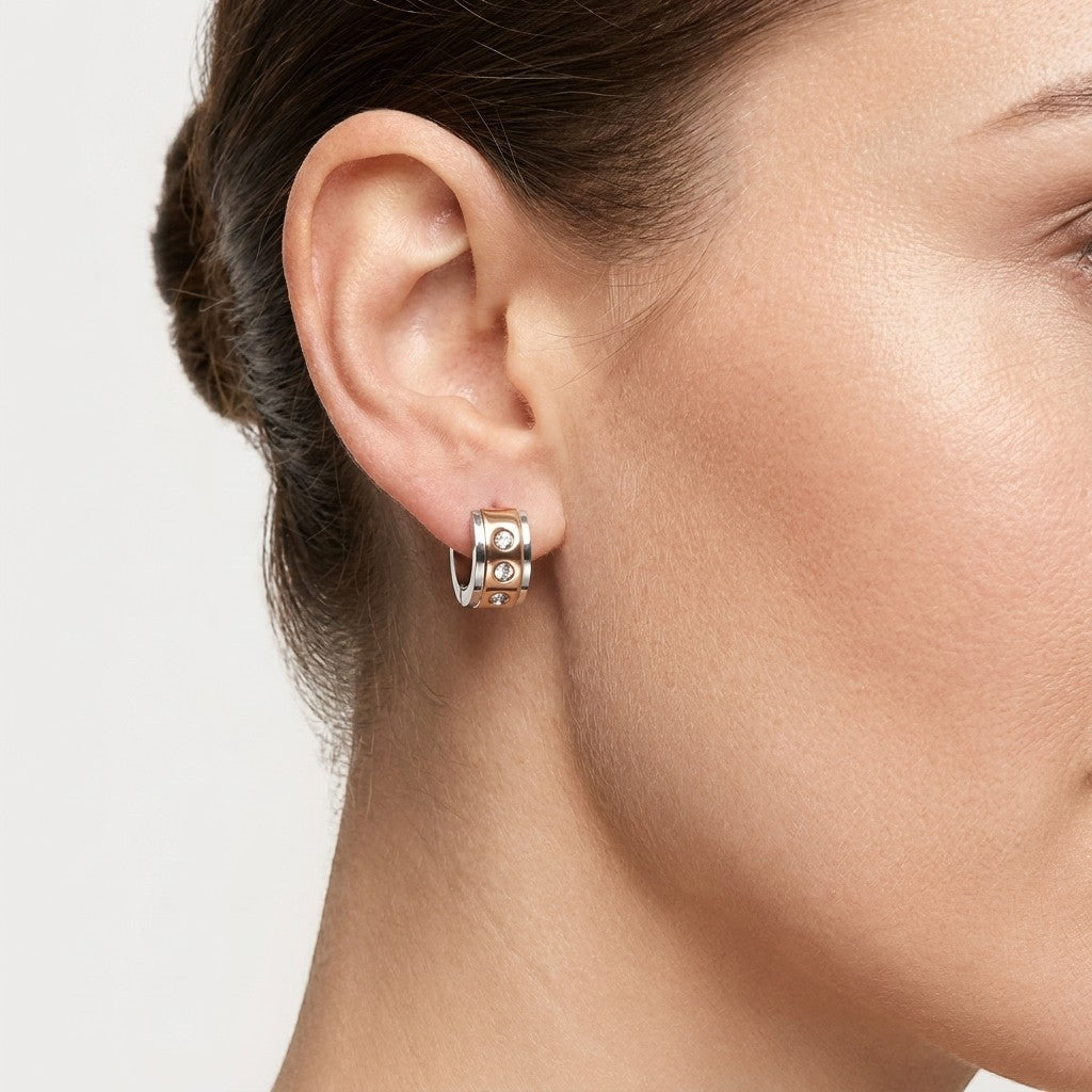 Aramat Jewels bicolor stainless steel huggie hoop earrings with three clear cubic zirconia stones on a woman's ear.