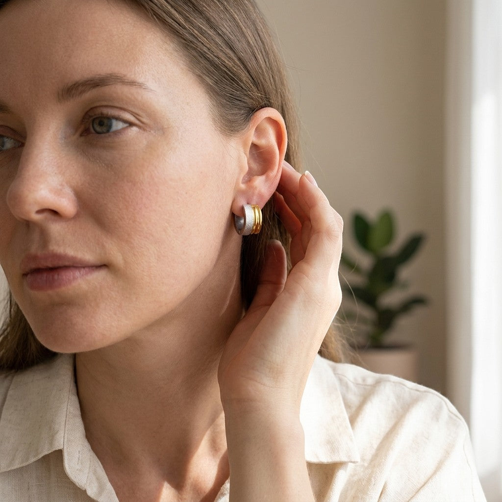 Aramat Jewels bicolor huggie hoop earrings in stainless steel with matte silver and shiny gold stripes, 13mm diameter.
