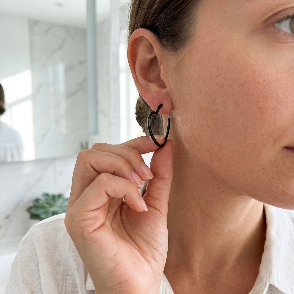 Aramat Jewels black heart-shaped hoop earrings, 20mm, made of stainless steel, worn by a woman.