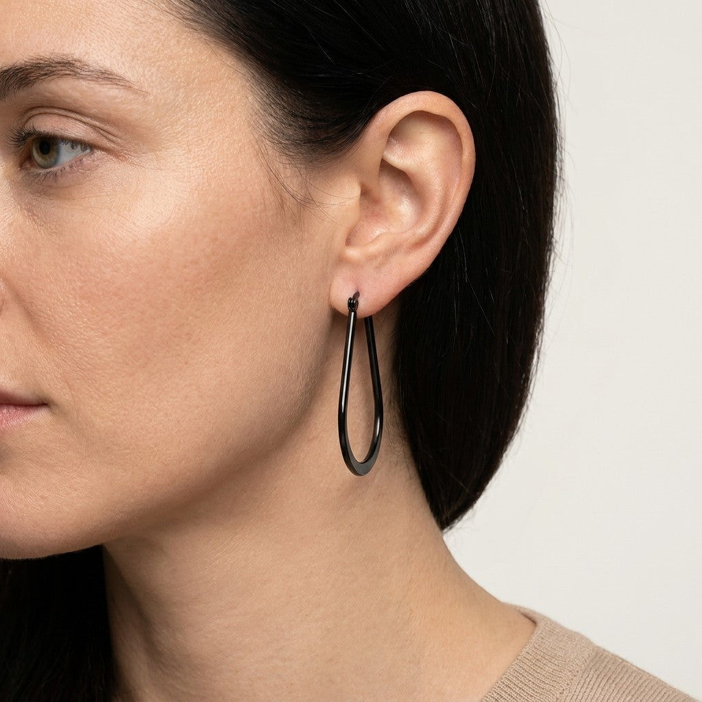 Aramat Jewels black oval hoop earrings with a glossy finish, worn by a woman.