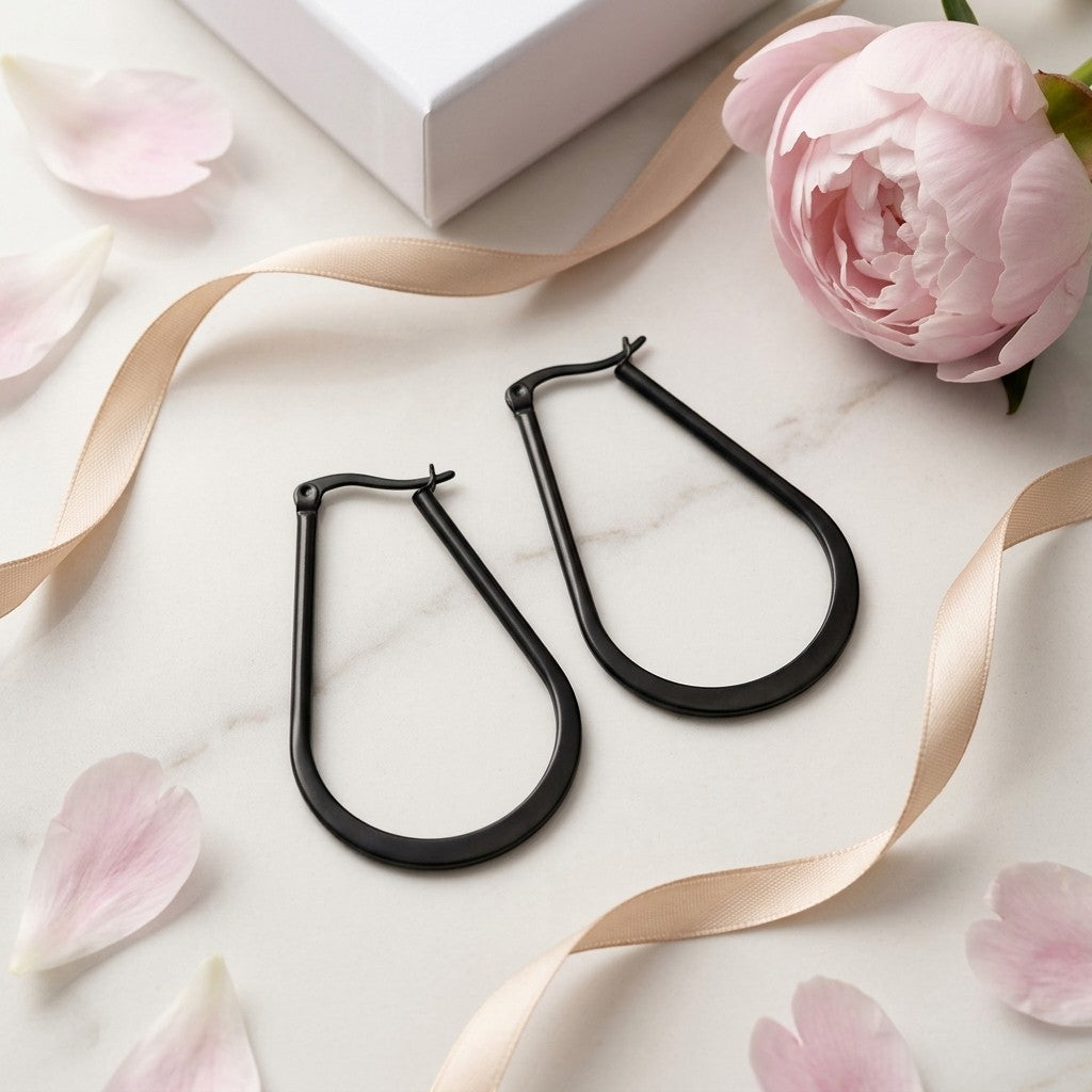 Aramat Jewels black oval hoop earrings made of steel with a shiny finish, styled with a ribbon and flower petals.