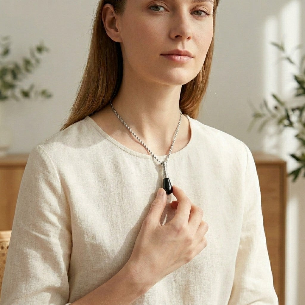 Aramat Jewels black and silver cone-shaped cremation urn pendant necklace made of 316L stainless steel, 4cm long, worn by a woman.