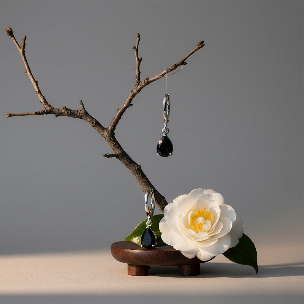 Aramat Jewels silver-tone mini hoop earrings with black teardrop zirconia stones, displayed on a branch with a white flower.