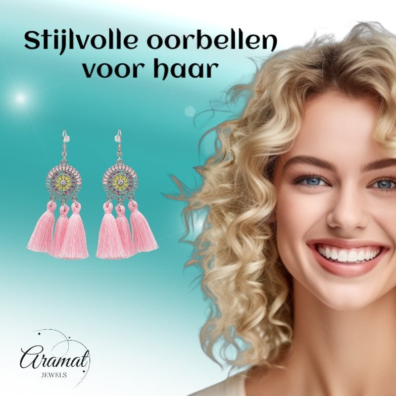 Aramat Jewels boho oorhangers met licht roze kwastjes en emaille details, gedragen door een lachende vrouw.