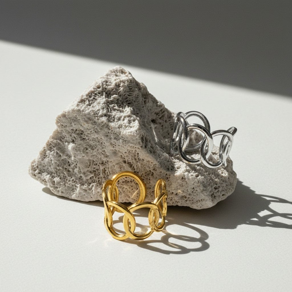Aramat Jewels brede verstelbare ringen van RVS met ovale schakels in goud- en zilverkleur op een rotsachtige ondergrond