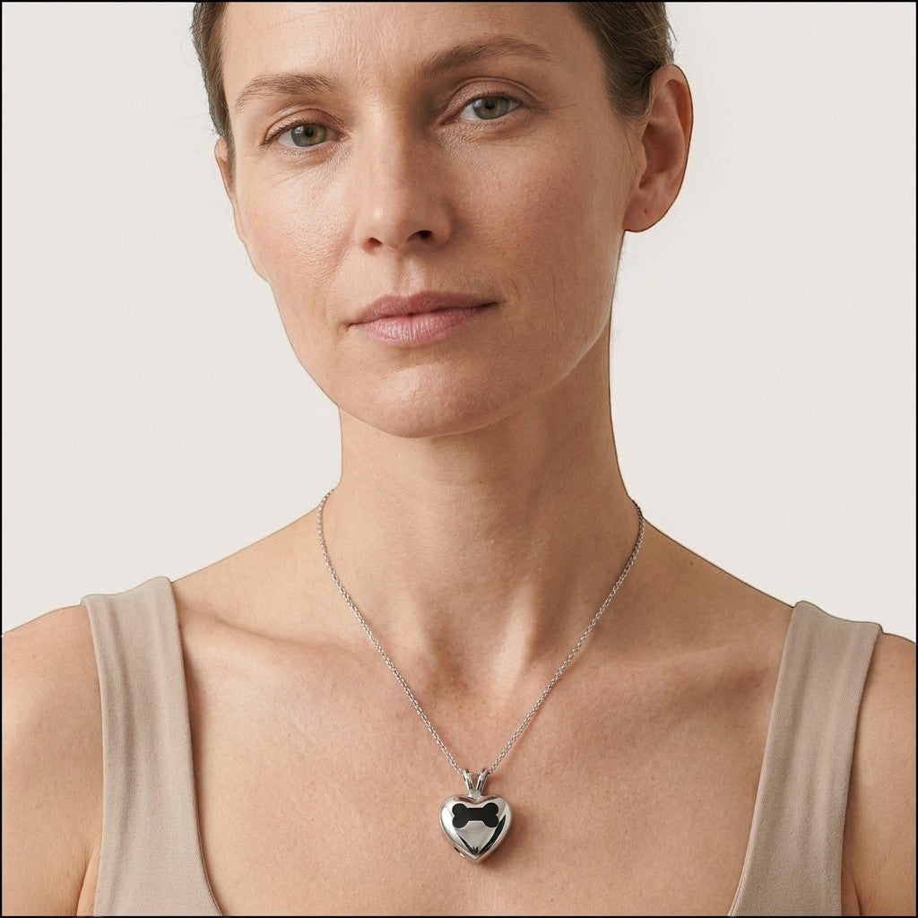 Aramat Jewels zilverkleurige stalen crematiehanger in hartvorm met een botdetail, gedragen door een vrouw.