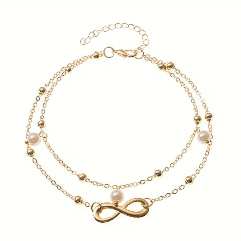 Aramat Jewels dubbel enkelbandje in goudkleur met infinity teken en witte parels voor een elegante zomerse look.