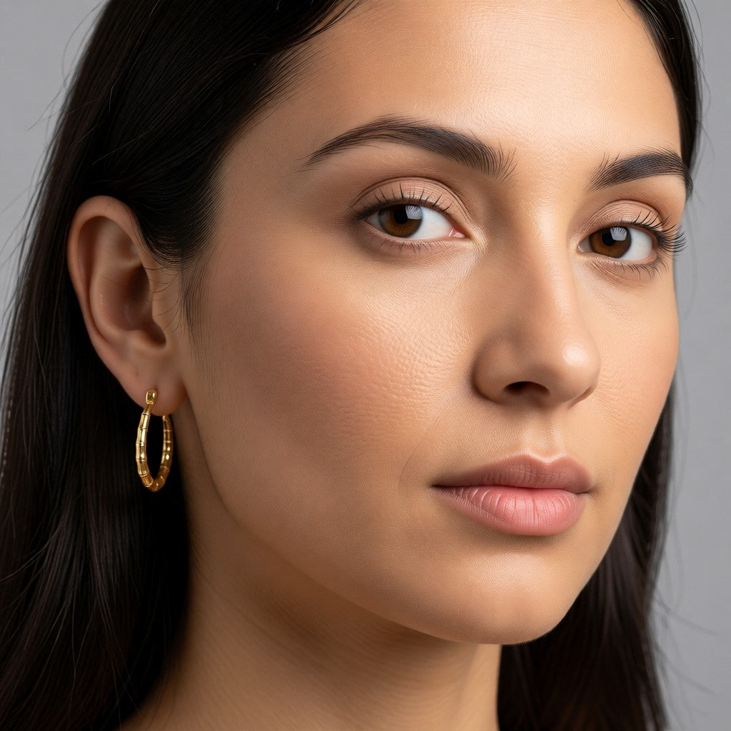 Aramat Jewels gold-coloured stainless steel hoop earrings with a bone-structure texture, 25mm diameter.