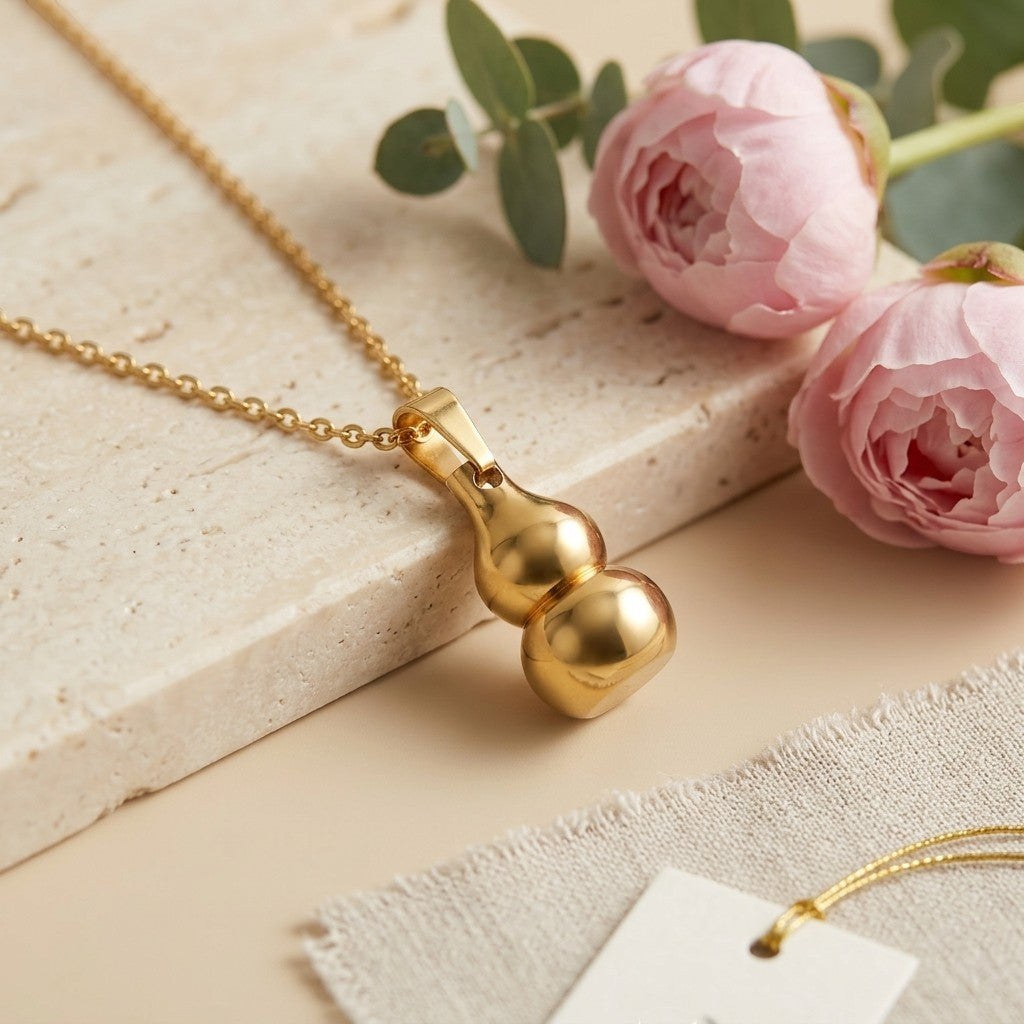 Aramat Jewels gold-colored gourd-shaped ash pendant on a delicate chain, symbolizing luck and protection. Made of stainless steel, 3x1.4cm.