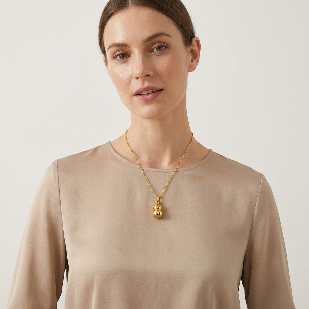Aramat Jewels gold gourd-shaped ash pendant necklace on a model. The stainless steel pendant is 3x1.4cm and holds ashes.