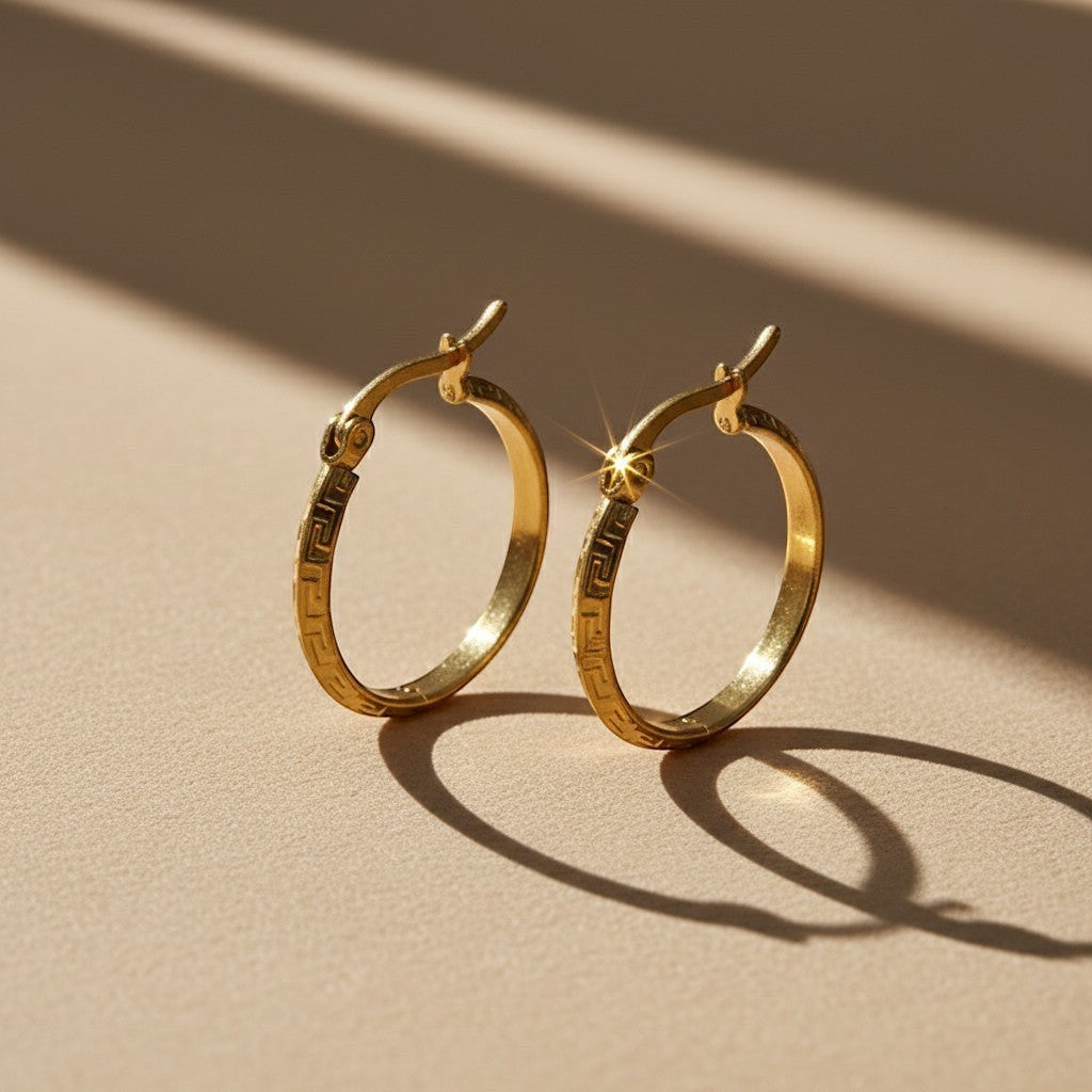 Aramat Jewels gold-tone stainless steel hoop earrings with Greek key pattern, 23mm diameter.