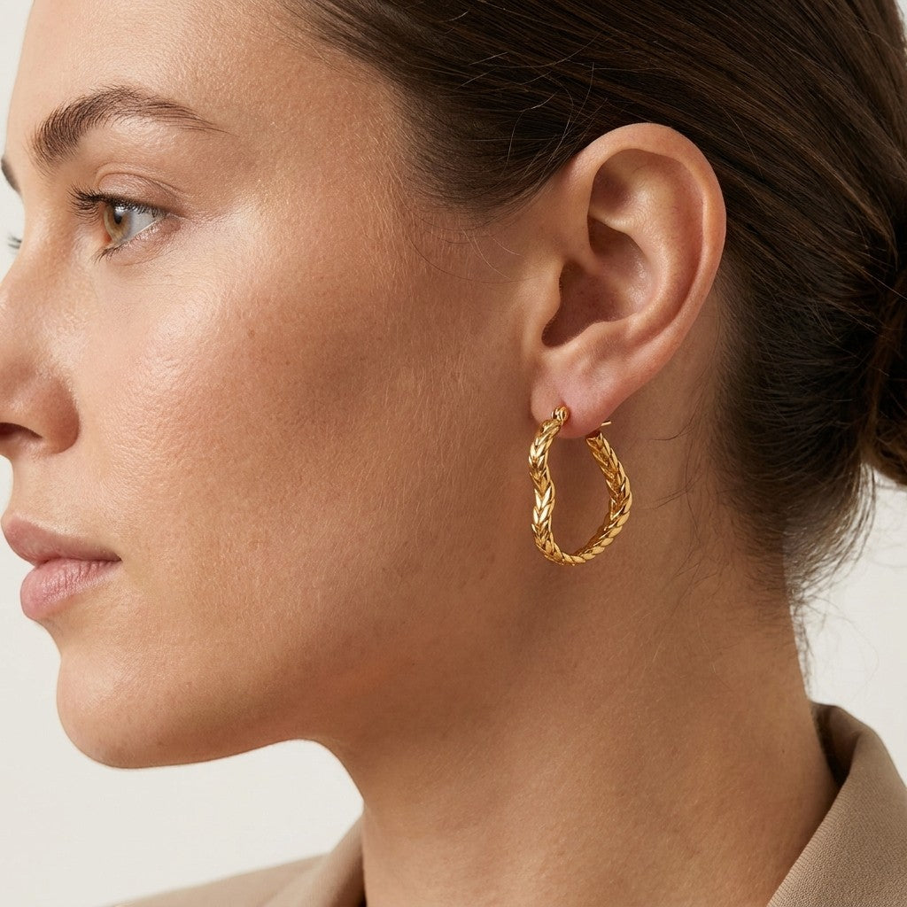 Aramat Jewels gold-tone heart-shaped hoop earrings with a gourmet link pattern, 25mm diameter, worn by a model.