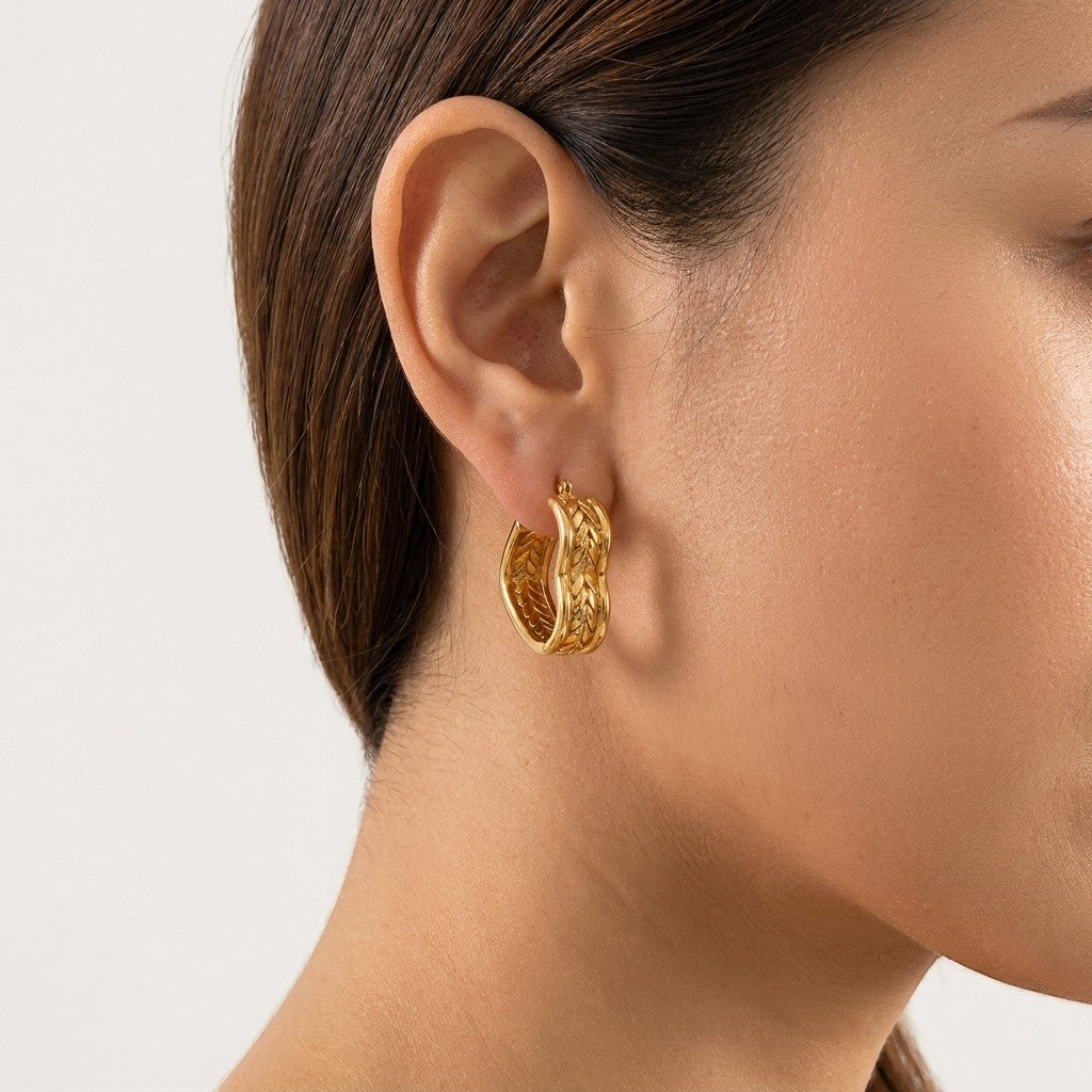 Aramat Jewels gold-tone stainless steel hoop earrings with a textured chain link design, worn by a woman.