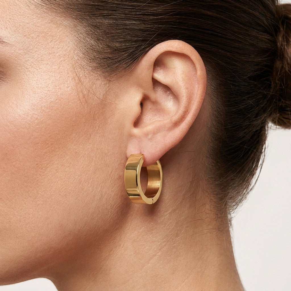 Aramat Jewels gold-coloured stainless steel hoop earrings, 20mm diameter, smooth polished finish, worn by a model.