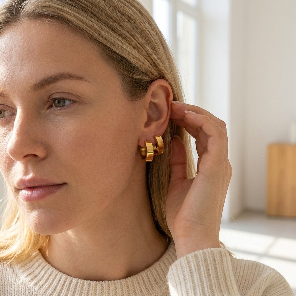Aramat Jewels gold-colored stainless steel hoop earrings, 20mm diameter, smooth finish, worn by a blonde woman.