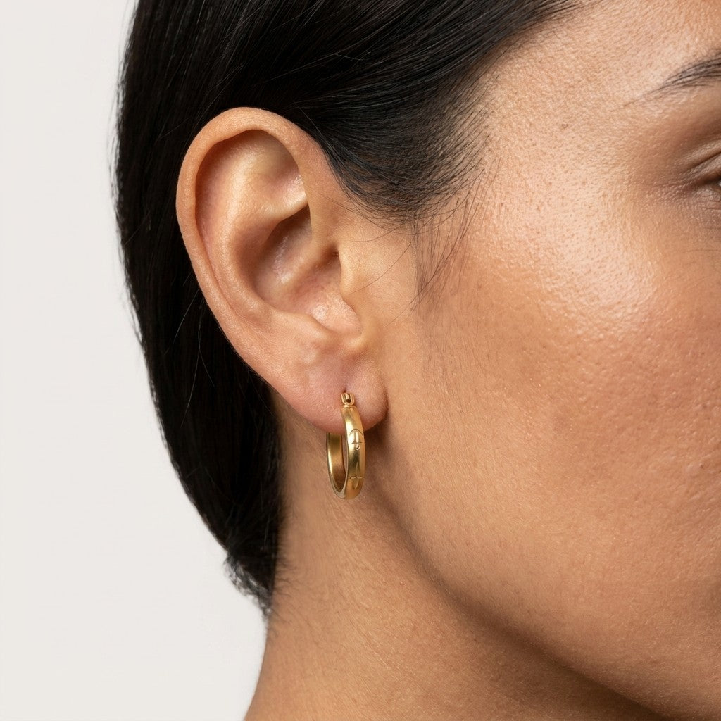 Aramat Jewels gold-tone 20mm stainless steel hoop earrings with anchor and star motif worn by a woman.