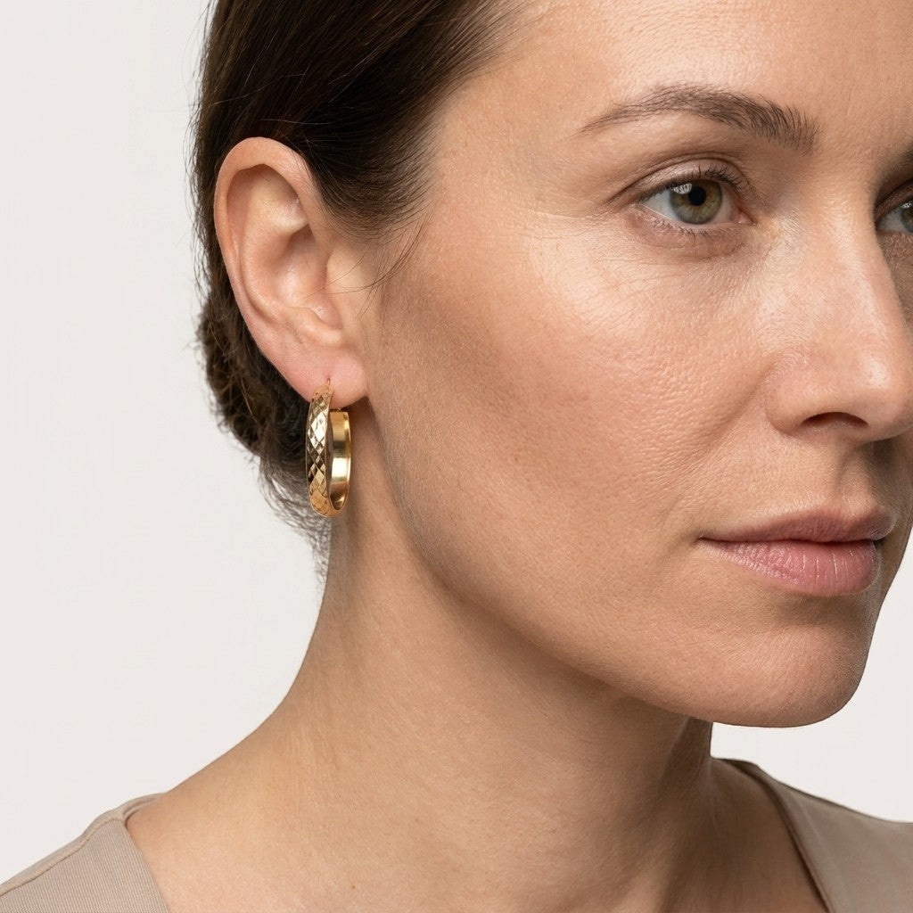 Aramat Jewels gold-tone stainless steel hoop earrings with a 35mm diameter and a checkered pattern, worn by a model.