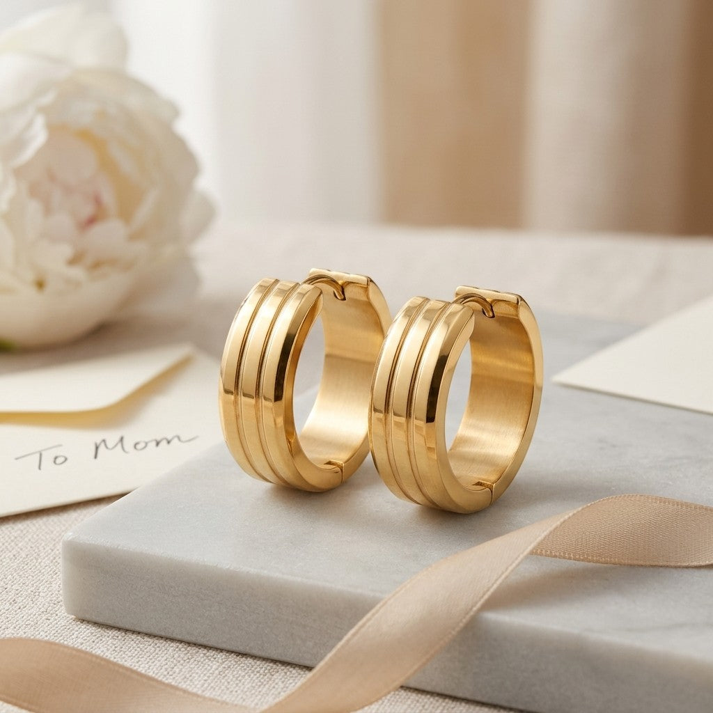 Aramat Jewels gold-tone stainless steel hoop earrings with double stripe detail. A white peony and a card saying 'To Mom' are in the background.