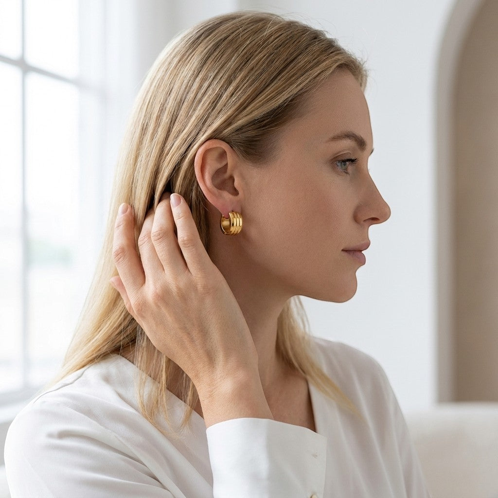 Aramat Jewels gold-tone stainless steel hoop earrings with double stripe detail, worn by a blonde woman.