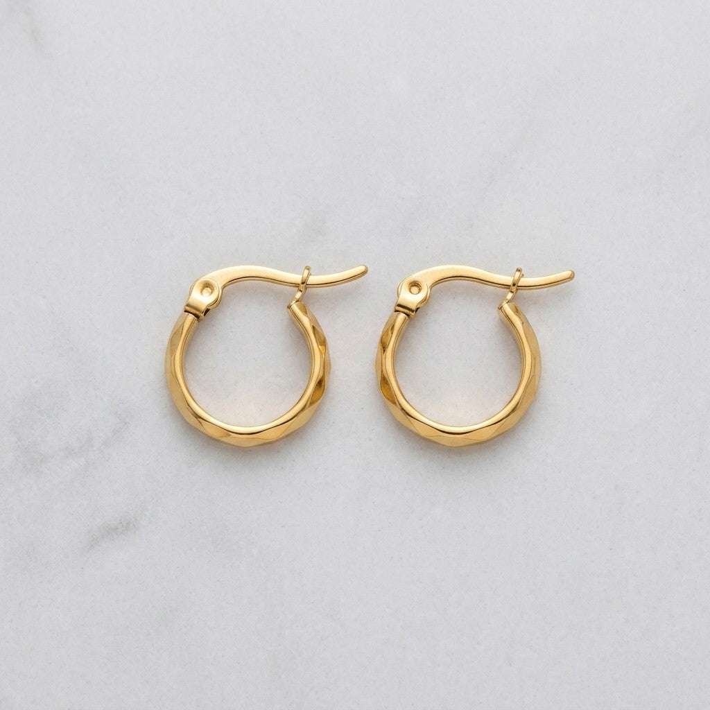 Aramat Jewels small gold-coloured stainless steel hoop earrings with faceted surfaces and a hinge closure.