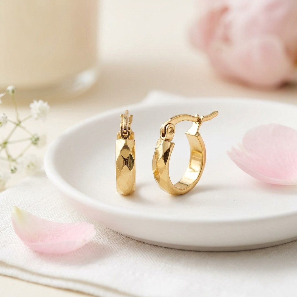 Aramat Jewels small gold-colored stainless steel hoop earrings with faceted surfaces and a hinge closure.