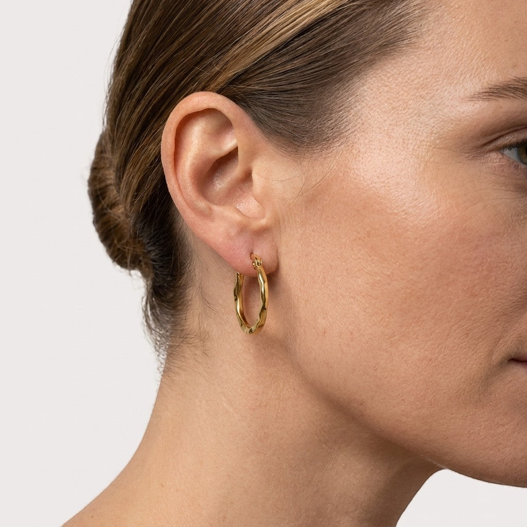 Aramat Jewels gold-coloured 20mm stainless steel hoop earrings with a fine stripe pattern, worn by a model.