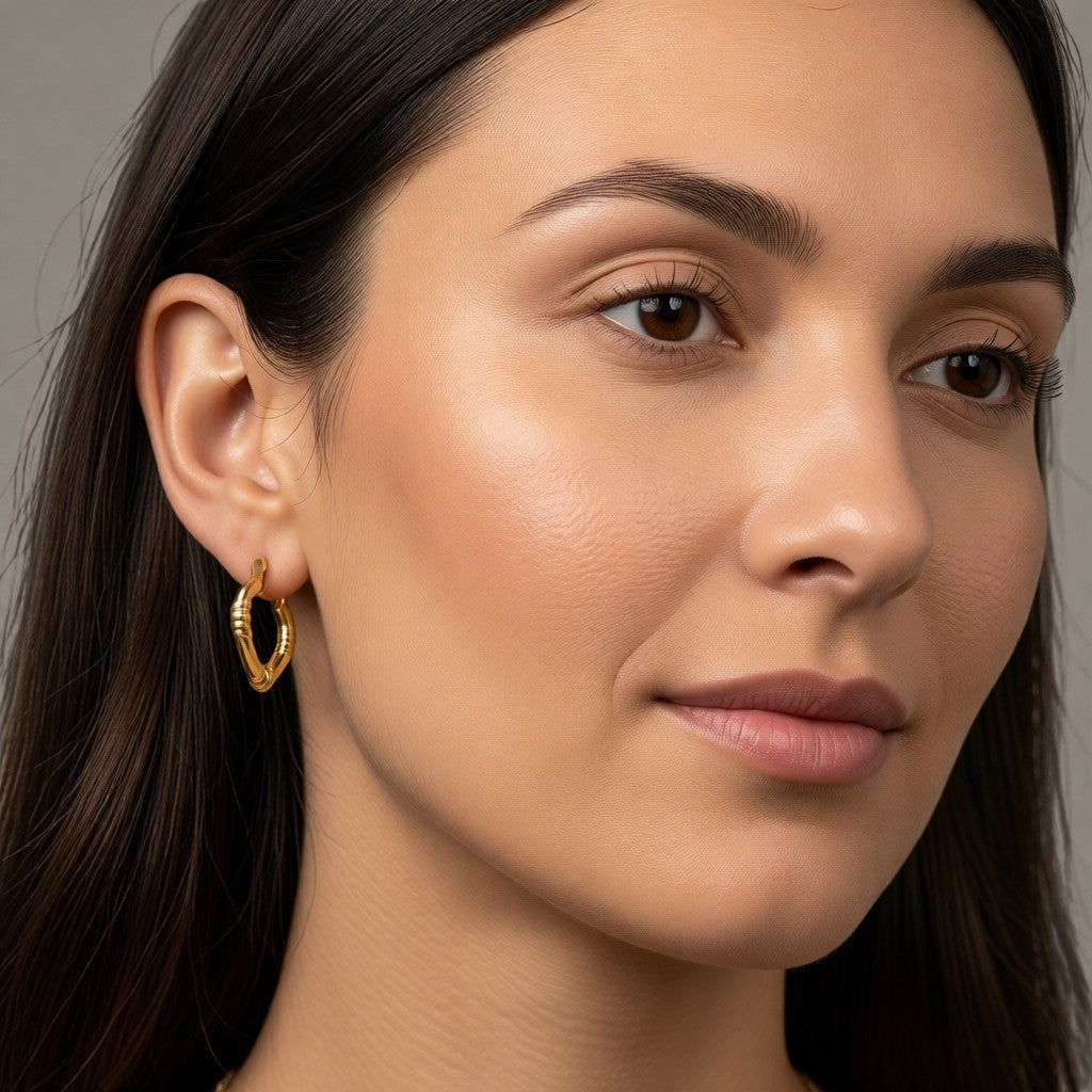 Aramat Jewels gold-coloured stainless steel hoop earrings with a subtle striped pattern, 22x20mm, worn by a model.