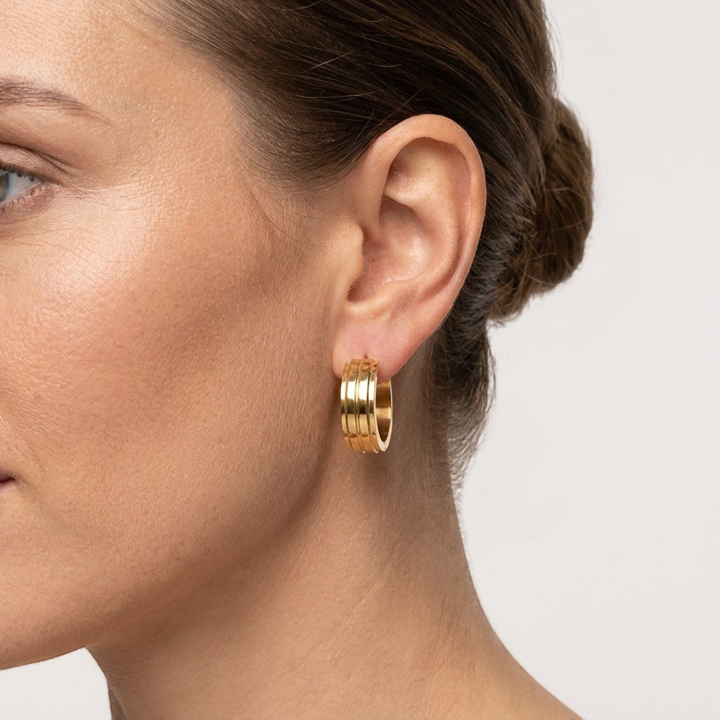 Aramat Jewels gold-tone stainless steel hoop earrings with three raised horizontal stripes, worn by a model.