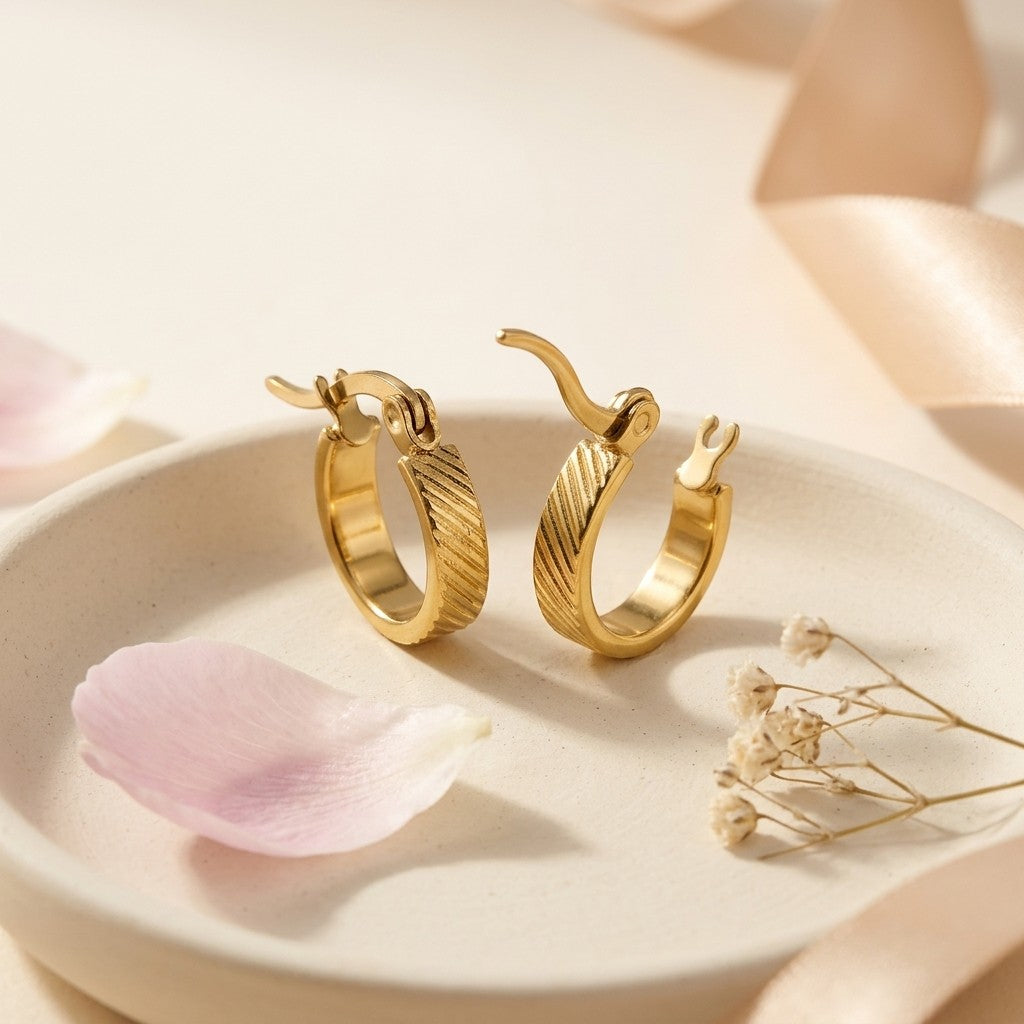Aramat Jewels small gold hoop earrings with a subtle striped pattern and hinge closure, made of stainless steel.