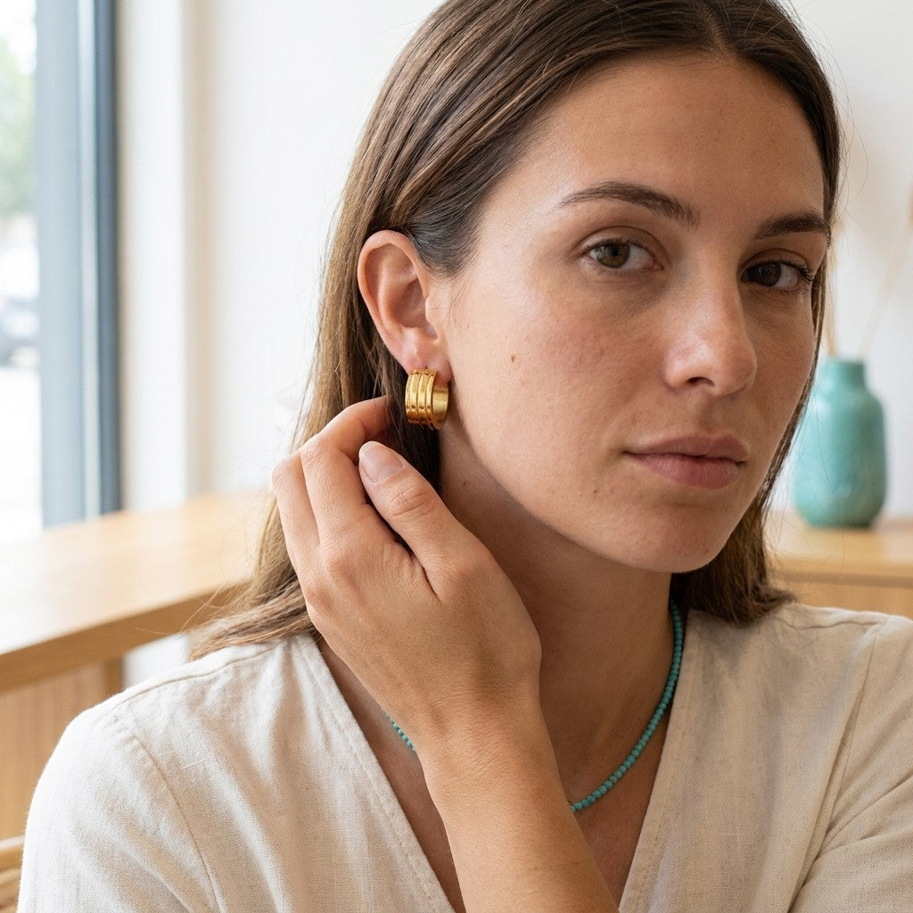 Aramat Jewels gold-tone stainless steel hoop earrings with two raised stripes, worn by a woman.