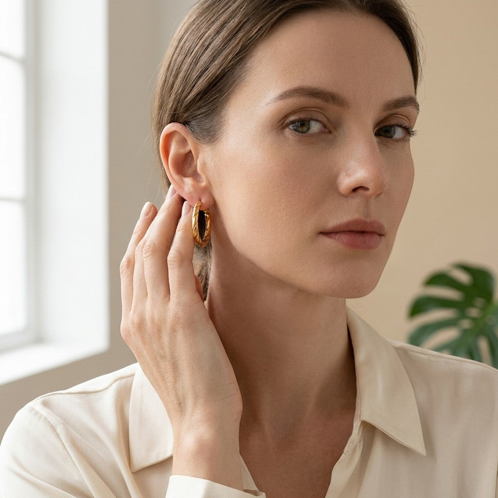Aramat Jewels gold-coloured stainless steel hoop earrings with a twisted rope motif, 25x3.5mm, worn by a woman.