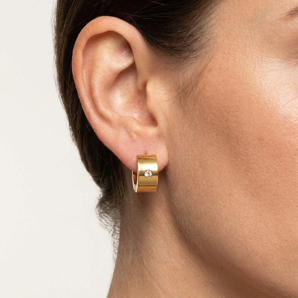 Aramat Jewels gold-coloured wide stainless steel hoop earrings with a single clear zirconia stone.
