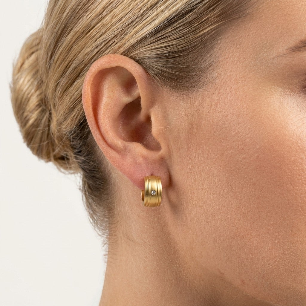 Aramat Jewels gold-plated RVS huggie hoop earrings with a small clear zirconia stone and ribbed texture.