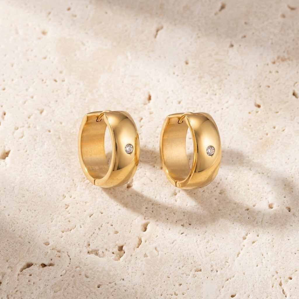 Aramat Jewels gold-tone stainless steel huggie hoop earrings with a central clear cubic zirconia stone.