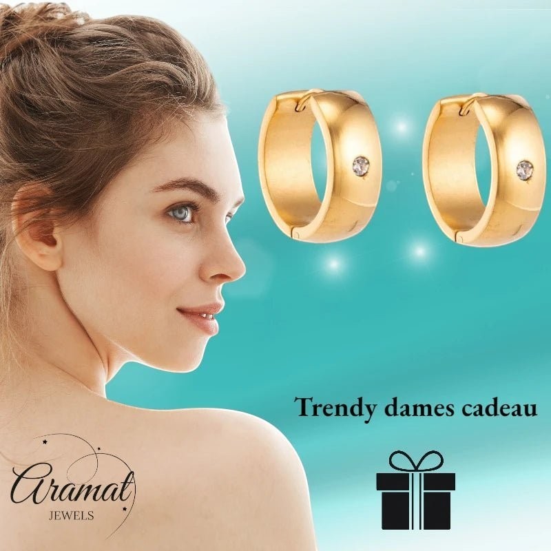 Aramat Jewels gold-tone stainless steel huggie hoop earrings with a central cubic zirconia stone, shown on a model.