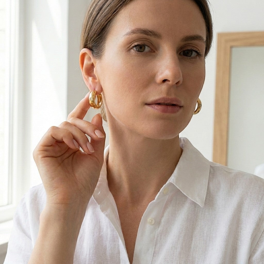 Aramat Jewels gold-tone stainless steel huggie hoop earrings with a central clear cubic zirconia stone.