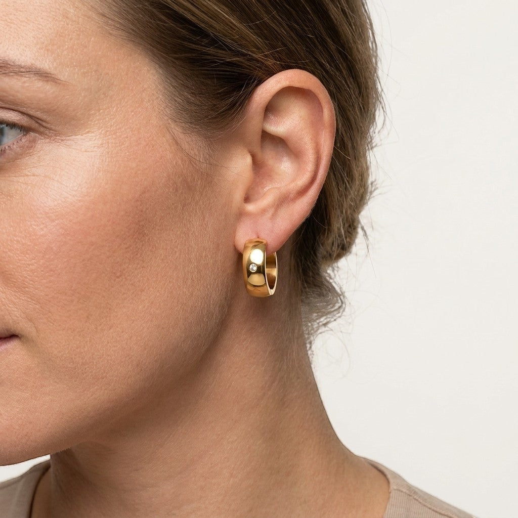 Aramat Jewels gold-tone stainless steel huggie hoop earrings with a central clear cubic zirconia stone.