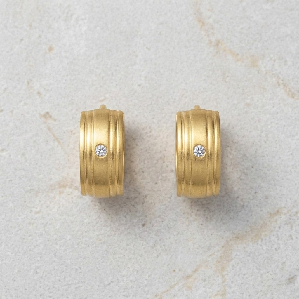 Aramat Jewels gold-tone stainless steel huggie hoop earrings with a single clear cubic zirconia stone and ribbed texture.