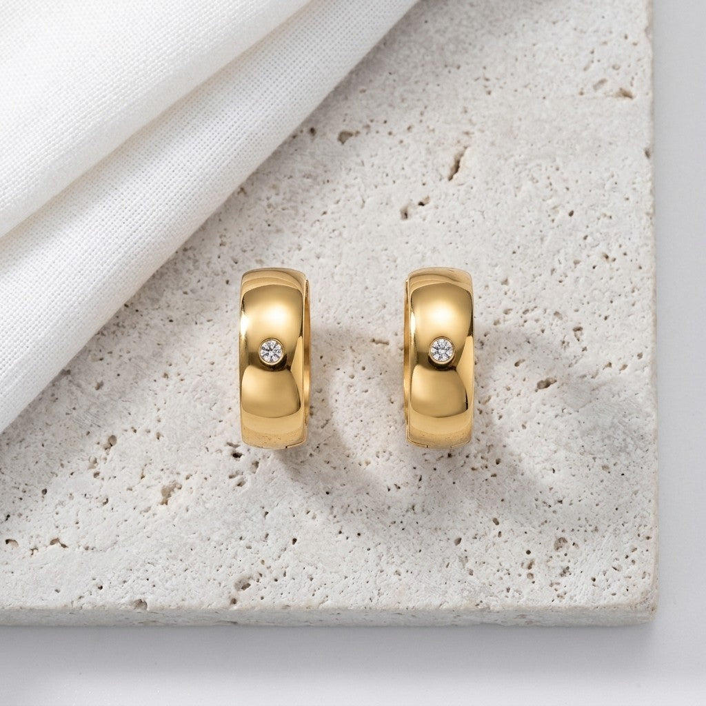 Aramat Jewels gold-tone stainless steel huggie hoop earrings with a central clear cubic zirconia stone.