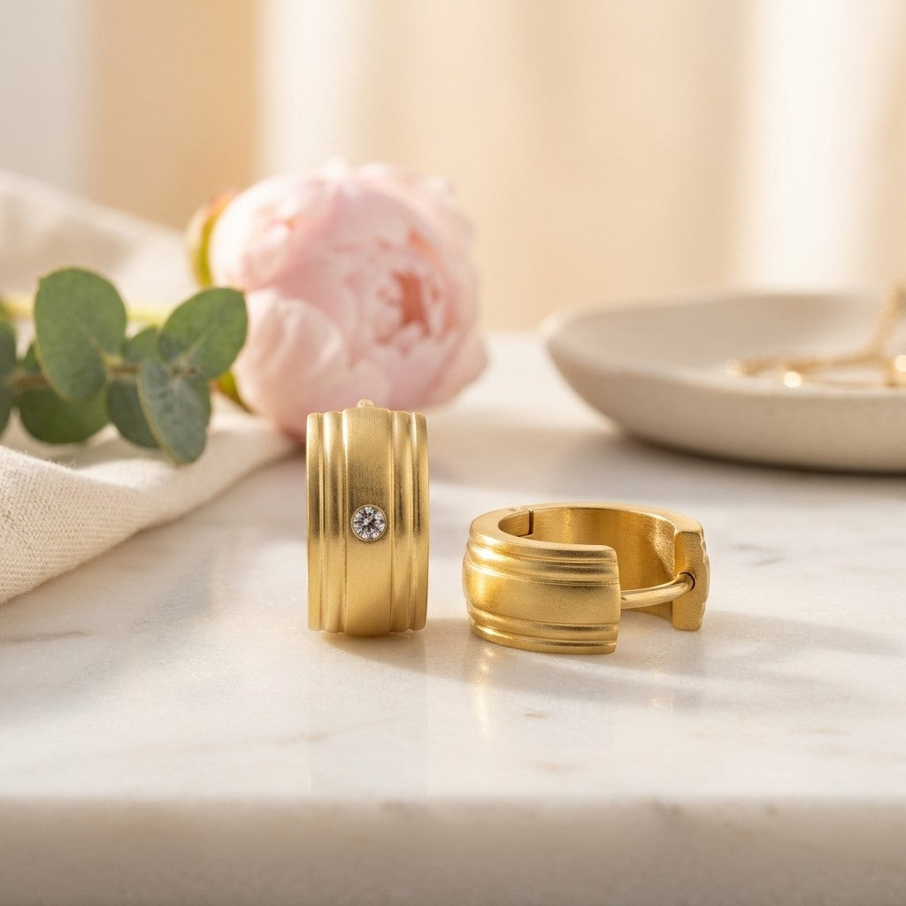 Aramat Jewels gold-tone stainless steel huggie hoop earrings with a small clear cubic zirconia stone and ribbed detailing.