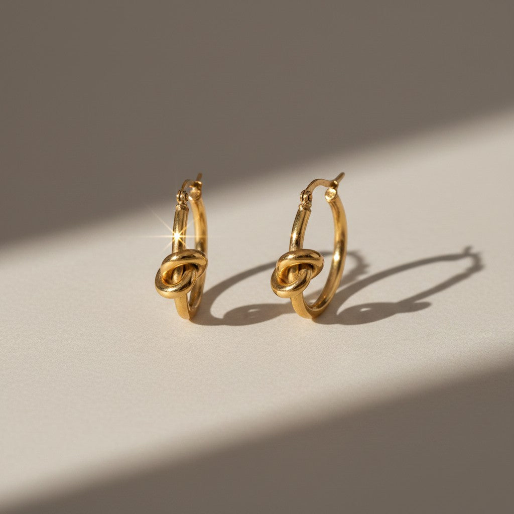 Aramat Jewels gold-tone stainless steel hoop earrings with a knot detail, 25mm diameter.