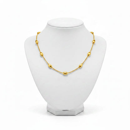 Aramat Jewels gold-colored stainless steel necklace with oval beads on a white display bust.