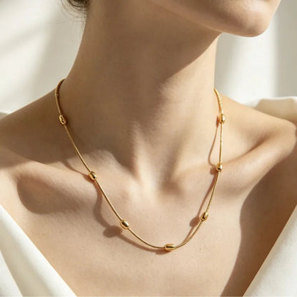 Aramat Jewels gold-colored stainless steel necklace with oval bead accents worn on a woman's neck