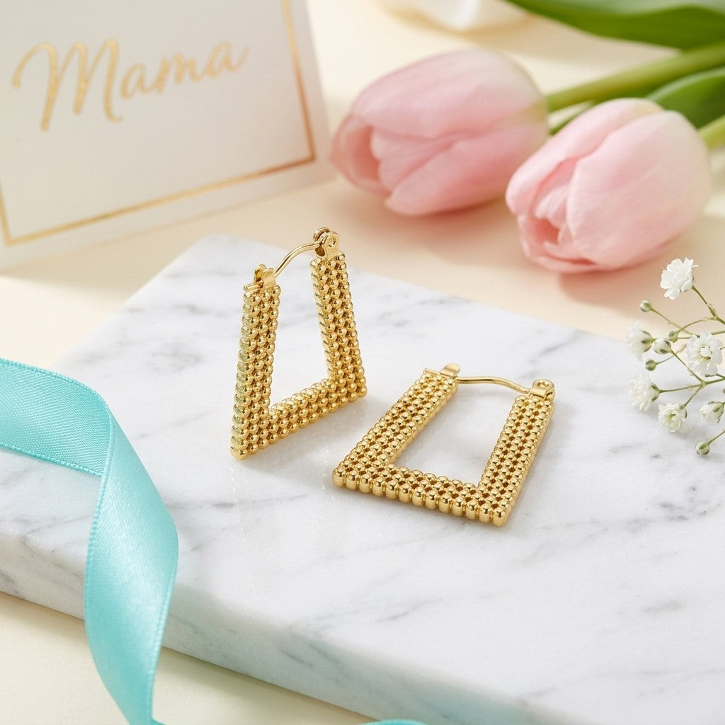 Aramat Jewels gold-tone stainless steel rectangular hoop earrings with a beaded texture, 28x20mm, styled on a marble surface with pink tulips.